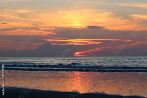 Landscape with dramatic sunrise over the Atlantic ocean in South Carolina  USA  Myrtle Beach area. Front view of calm ocean rippling waves and sunlight reflection in low tide.