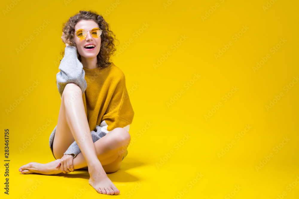 Colorful fashion modern beauty sexy skinny women female adult model wearing  yellow long hoody sweater and sunglasses isolated on solid yellow background  at studio. Beauty and summer fashion concept. Stock Photo |