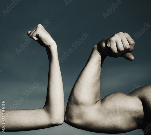 Muscular arm vs weak hand. Vs, fight hard. A heavily muscled man arm wrestling a puny weak man. Competition, strength comparison. Health concept. Hand, man arm, fist. Close-up. Black and white.