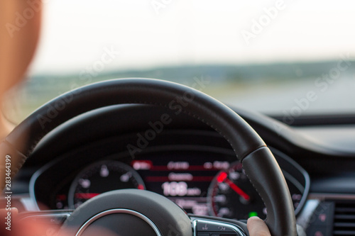 Young man wearing a red t-shirt driving a beautiful car at high speed. Close up steering wheel with blurred light beige salon background © OlhaL
