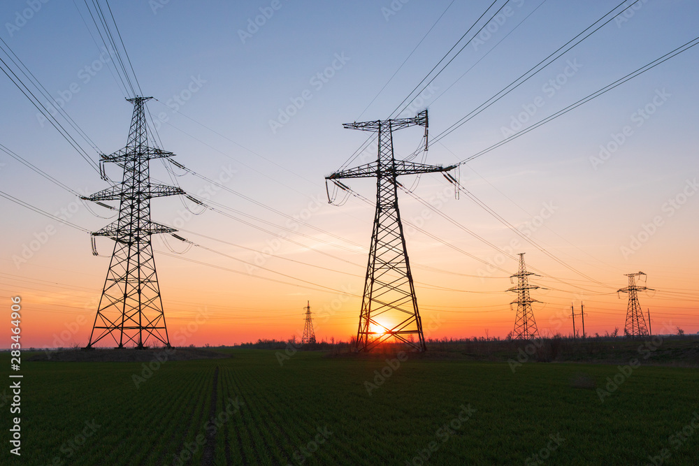 High voltage lines and power poles and green agricultural landscape during sunrise.