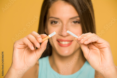 Young happy woman holding a broken cigarette on yellow background