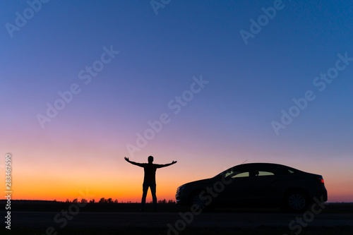Silhouette of a man and a car on a background of a very beautiful sunset. Freedom and travel by car concept.