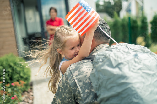 Daughter holding little American flag hugging daddy tight
