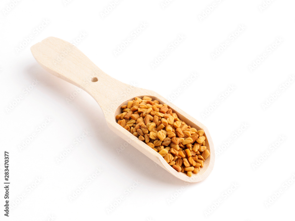 Fenugreek (Trigonella) in a wooden scoop on a white background diagonally Fenugreek (Trigonella) in a wooden scoop on a white background diagonally