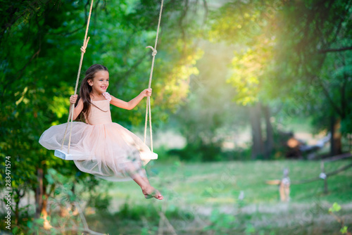 Happy girl rides on a swing in park. Little Princess has fun outdoor, summer nature outdoor. Childhood, child lifestyle, enjoyment, happiness.