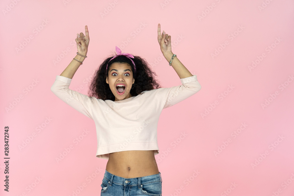 Amazed shocked young african american woman point fingers up at copy space look at camera, surprised excited black teen girl show upward advertise fashion sale isolated on studio pink background Amazed shocked young african american woman point fingers up at copy space look at camera, surprised excited black teen girl show upward advertise fashion sale isolated on studio pink background