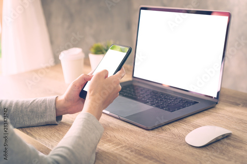 Hipster women holding phone and using laptop on wooden table in coffee shop.