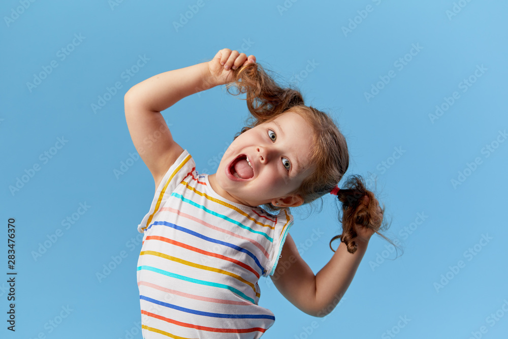 Portrait of surprised smiling cute little toddler girl. child standing isolated over blue background. Looking at camera and laughs
