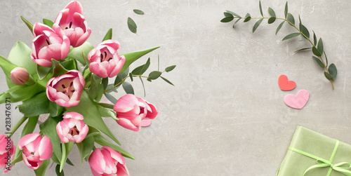 Springtime flat lay with bunch of pink tulips, eucalyptus leaves and gift boxes on stone