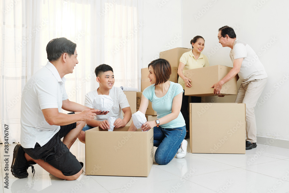 Cheerful big Vietnamese family packing belongings in cardboard boxes to move out Cheerful big Vietnamese family packing belongings in cardboard boxes to move out