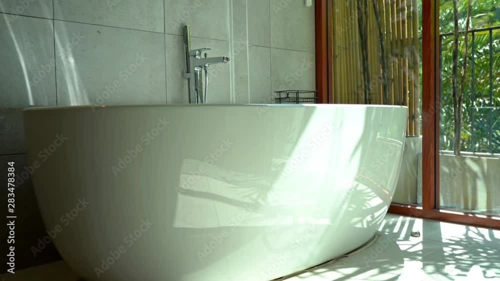 Slow pan left on ceramic rounded bathtub in bathroom with ceiling to bloor window Slow pan left on ceramic rounded bathtub in bathroom with ceiling to bloor window