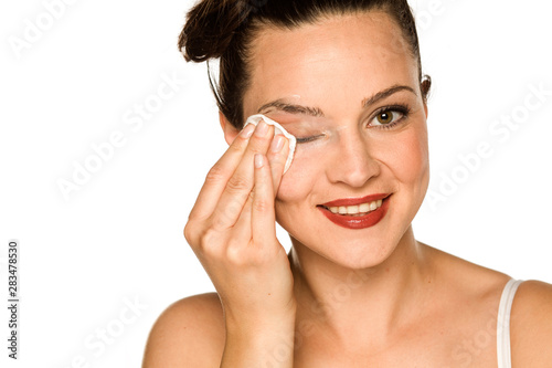 young happy woman cleans her face with cotton pad on white background