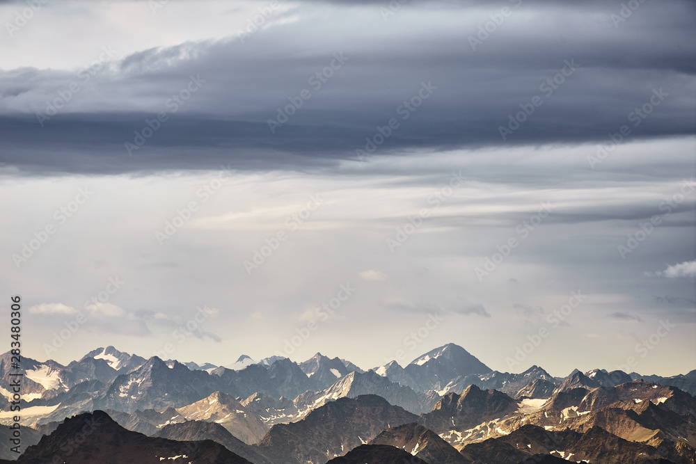 View over the Austrian and Swiss Alps from the Zugspitze, with a dramatic sky over the rugged mountains.