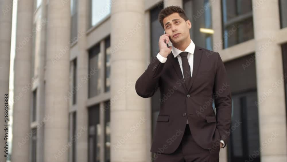 Lockdown of young attractive mixed-race man wearing elegant suit standing outdoors and having phone conversation Lockdown of young attractive mixed-race man wearing elegant suit standing outdoors and having phone conversation