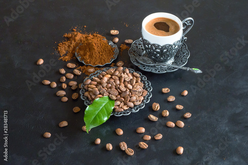 Cup of coffee and coffee beans with ground powder on black background