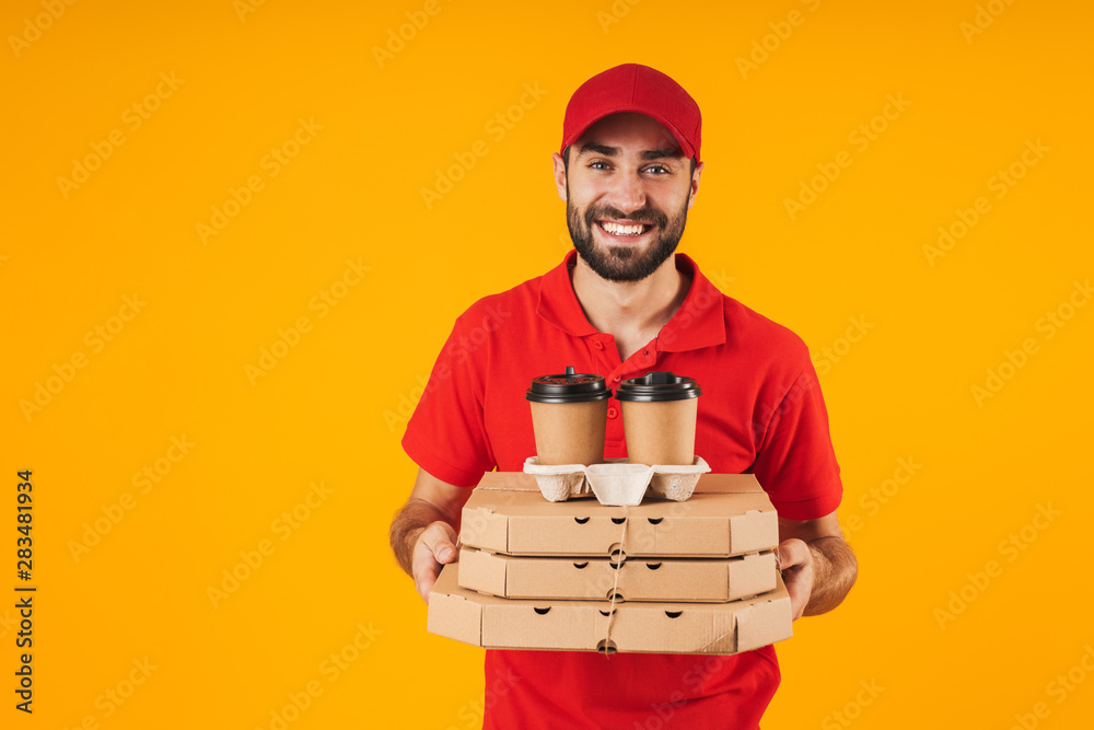 Portrait of smiling delivery man in red uniform holding pizza boxes and takeaway coffee Portrait of smiling delivery man in red uniform holding pizza boxes and takeaway coffee