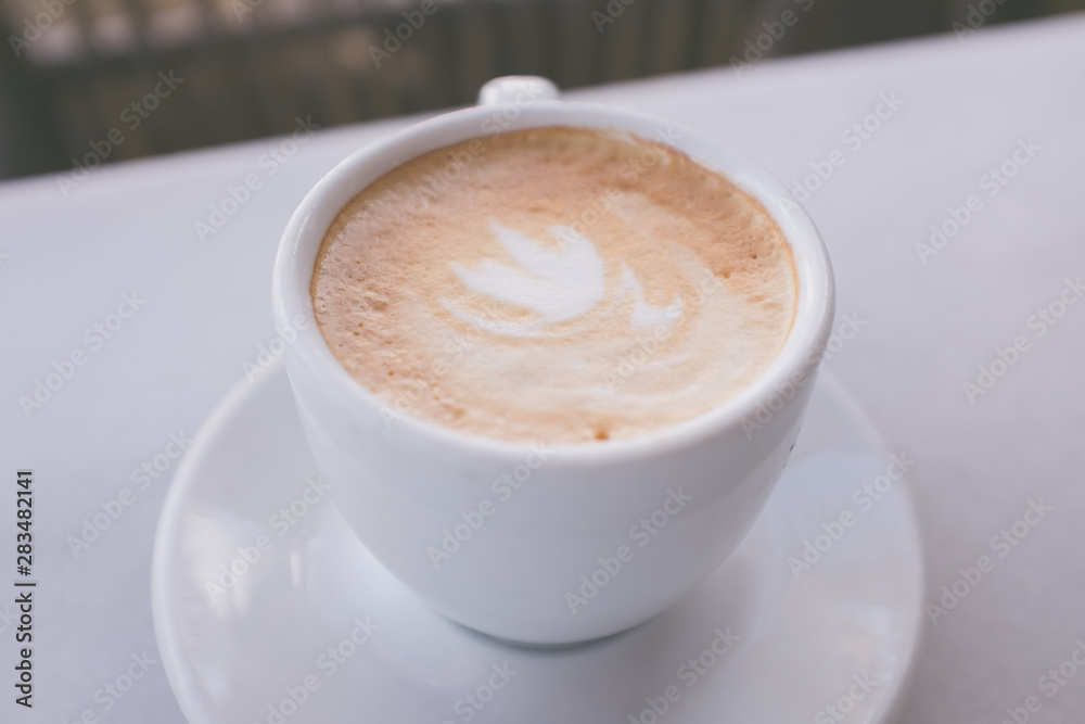 Cup of coffee with milk on marble table with wooden chairs in unfocused background, vintage style Cup of coffee with milk on marble table with wooden chairs in unfocused background, vintage style