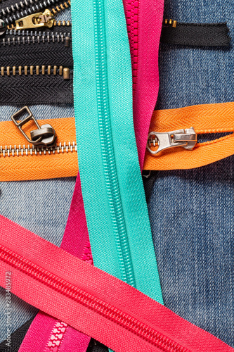 Pack a lot of colorful plastic and metal zippers stripes with sliders pattern for handmade sewing tailoring on the blue denim background close up selective focus