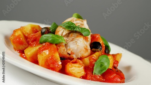 Traditionally prepared cod in Spanish. Served in tomato sauce with boiled potatoes, olivki and basil. Front view.  Food presentation. Turning the platter. photo