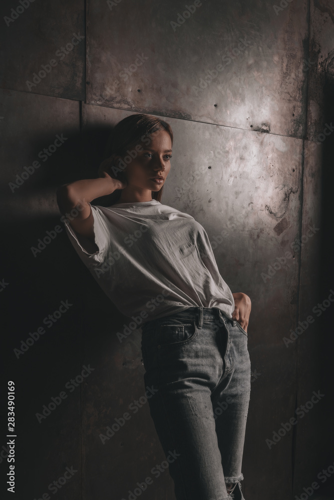Sexy hot woman in white shirt and jeans posing in loft studio on metallic wall background. Seductive glamour young girl model portrait.
