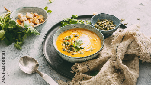 Pumpkin soup in a bowl garnished with pumpkin seed and fresh herbs.