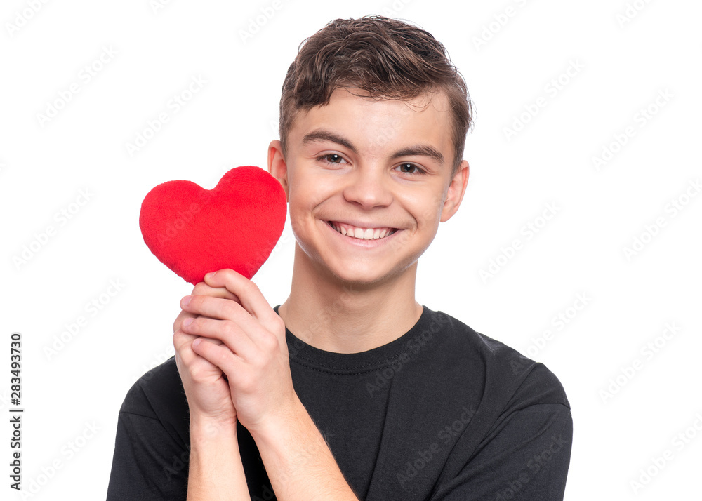 Valentines Day concept. Portrait of cute teen boy with red heart, isolated on white background. Smiling boy holding symbol of love, family, hope. Cute caucasian teenager holding plush heart in hands. Valentines Day concept. Portrait of cute teen boy with red heart, isolated on white background. Smiling boy holding symbol of love, family, hope. Cute caucasian teenager holding plush heart in hands.