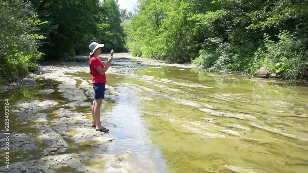 walks in the wild on a sunny summer day.young woman on a walk on the shore of a mountain river.girl takes pictures of the surrounding space on a modern electronic device. walks in the wild on a sunny summer day.young woman on a walk on the shore of a mountain river.girl takes pictures of the surrounding space on a modern electronic device.