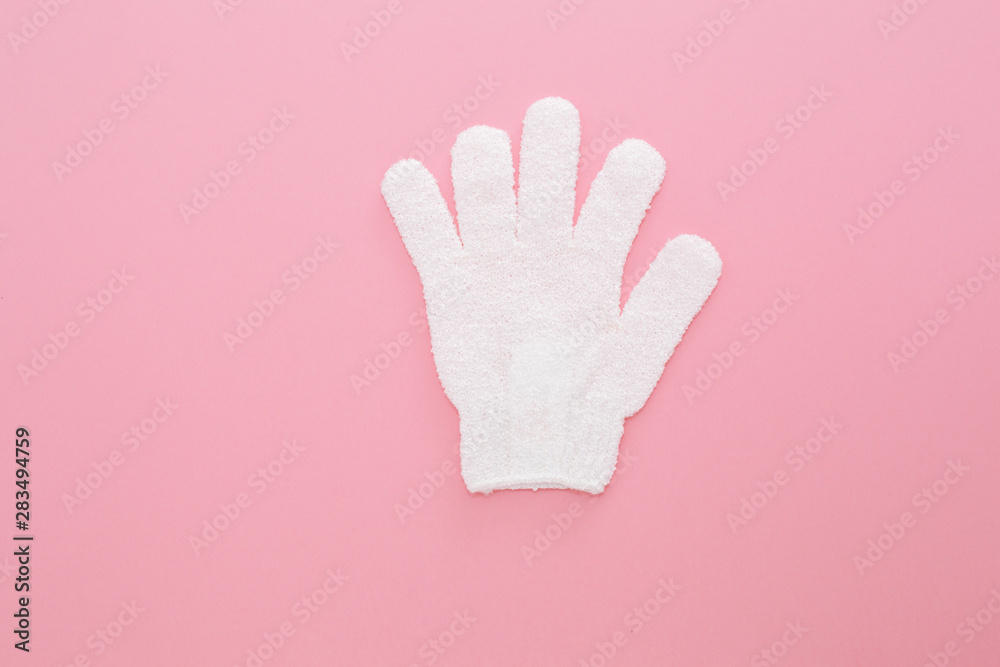 Obraz premium Woman exfoliating massage glove for shower on pink background.Gloves for use in the shower for massage and scrub. Beauty background with cosmetic products. Beauty, health and spa concept