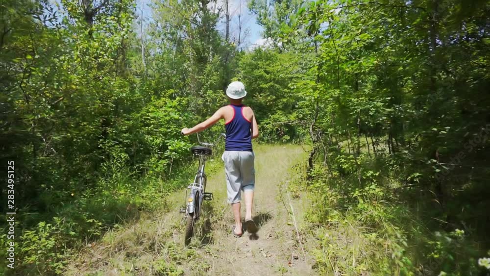 summer time.summer rest.holidays.hiking.camera follows the teenager boy.school age boy who goes holding bicycle.forest walk on a sunny summer day summer time.summer rest.holidays.hiking.camera follows the teenager boy.school age boy who goes holding bicycle.forest walk on a sunny summer day