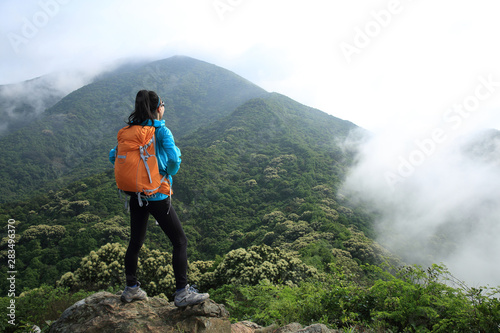Successful young woman backpacker on forest mountain top looking at the view