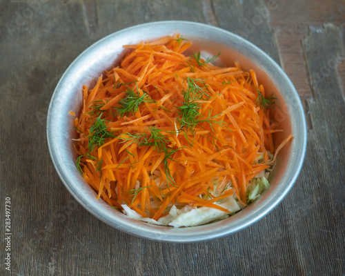 Harvesting for vitamin salad of cabbage and grated carrots in an aluminum plate, removed from close range
