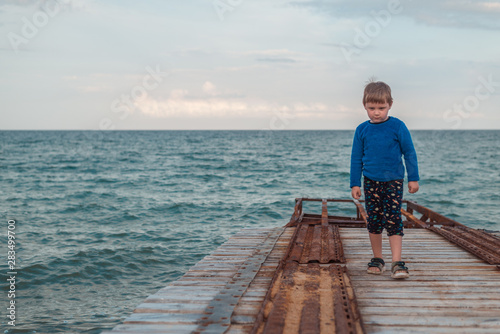 A little boy is walking along the pier to the sea, the ocean.