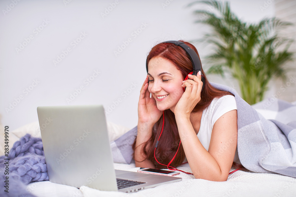 the student is happy to communicate with friends via the Internet. home schooling, work and study, new knowledge.happy teen on bed with computer. girl student lying on the bed smiling. the student is happy to communicate with friends via the Internet. home schooling, work and study, new knowledge.happy teen on bed with computer. girl student lying on the bed smiling.