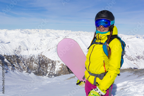 Girl with a snowboard posing at the panorama of the mountains.