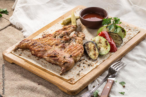 Chicken tobacco on a wooden Board with grilled vegetables and tomato sauce on tablecloth photo