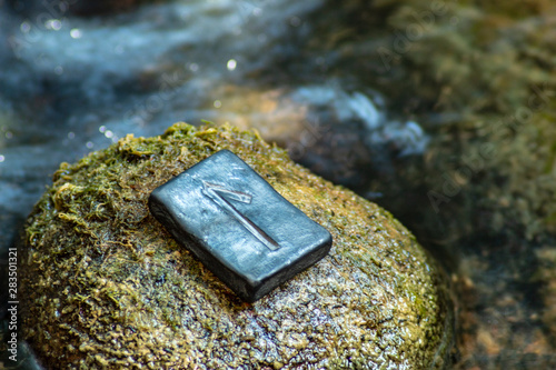 Norse rune Laguz (Laukr) on the stone and the evening river background. Love, youth, intuition, mysticism, magic. Water, flow, life.