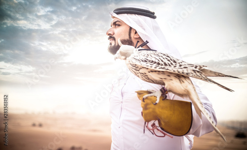 Arabic man with traditional emirates clothes walking in the desert with his falcon bird photo