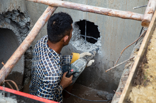 The builder with a hammer  making hole in wall at construction the wall, drains into the hands of workers.