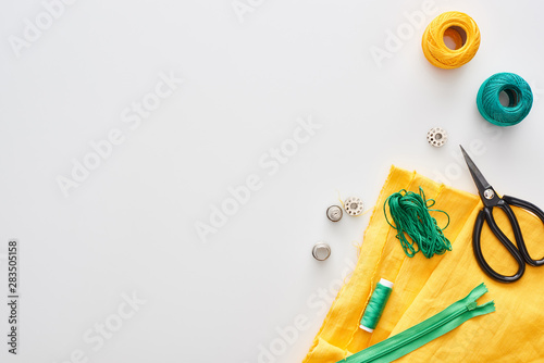 top view of zipper  scissors  thimbles  threads  knitting yarn balls  bobbins  fabric on white background