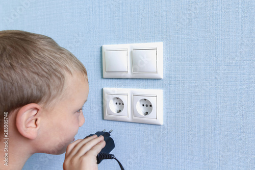 Kid playing with electrical outlet. Curious little boy with a wire in hands. Danger to children photo