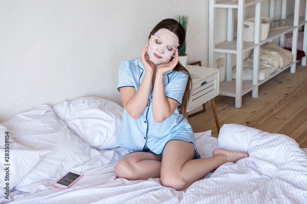 Beautiful fit brunette woman at home in pajama. She do beauty procedures - apply face moisturizing mask. Natural light. Lifestyle healthcare concept Beautiful fit brunette woman at home in pajama. She do beauty procedures - apply face moisturizing mask. Natural light. Lifestyle healthcare concept