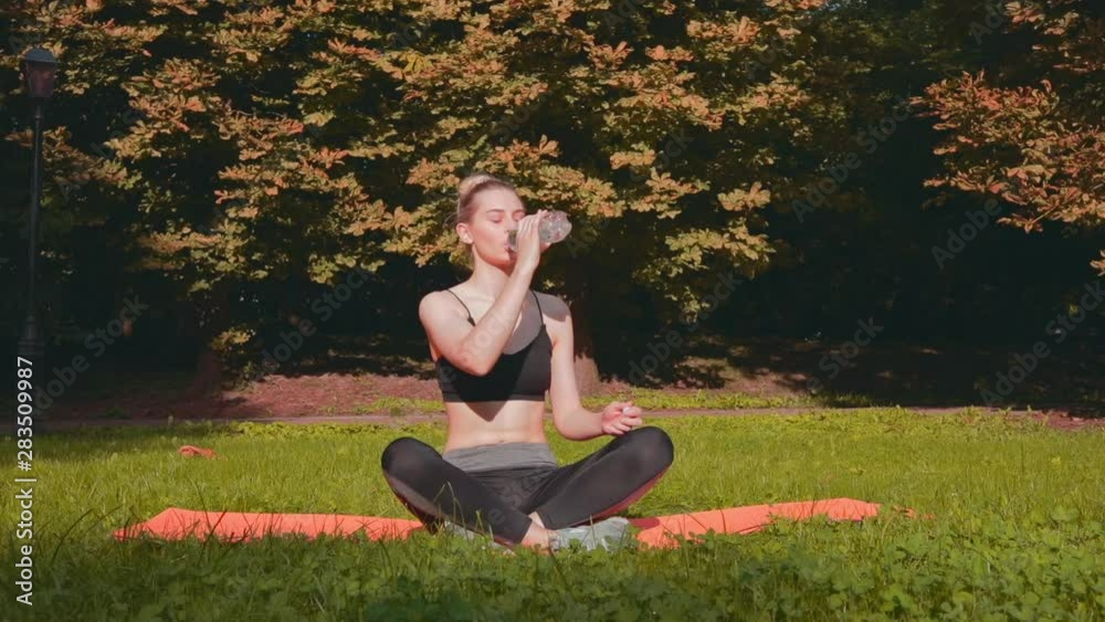 Young sporty girl drink water in morning sunny park. Woman doing yoga in the park. Athlete woman doing stretching exercise in summer park. Healthy sports lifestyle. Young sporty girl drink water in morning sunny park. Woman doing yoga in the park. Athlete woman doing stretching exercise in summer park. Healthy sports lifestyle.