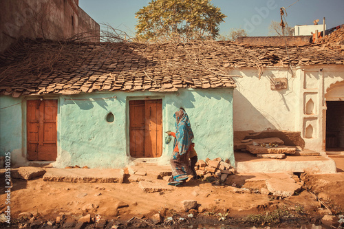 People walking past small traditional indian village house. Colorful buildings of rural area in India