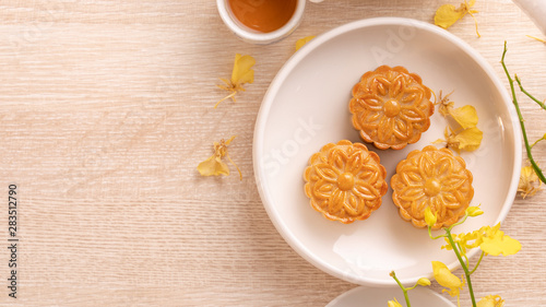 Tasty moon cake for Mid-Autumn festival on bright wooden table  concept of festive afternoon tea decorated with yellow flowers  top view  flat lay.