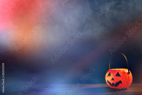 Halloween concept - Orange plastic pumpkin lantern on a dark wooden table with blurry sparkling light in the background, trick or treat, close up.