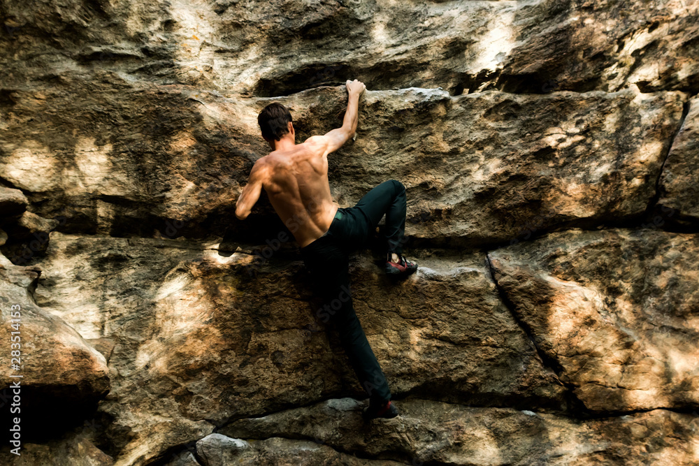 Rock climber climbs bouldering on a cliff on forest. Low angle of strong rock climbing man hanging free on rock with sunflare Rock climber climbs bouldering on a cliff on forest. Low angle of strong rock climbing man hanging free on rock with sunflare