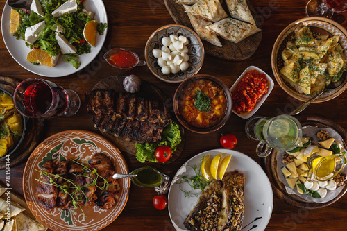 delicious dishes of Ukrainian and Georgian national cuisines placed on a large wooden table: meat, fish, adzhika, booze, salad, fried potatoes, cheese