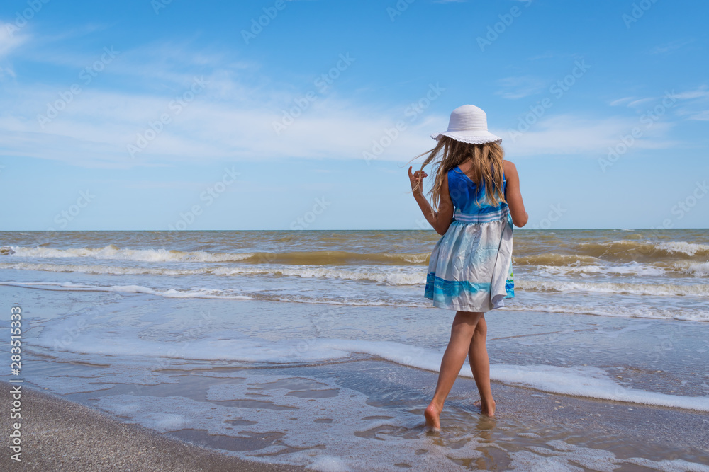 Beautiful girl in white hat and colorful dress on the seashore over blue sky background