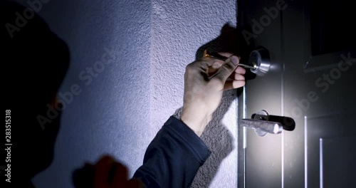 burglar trying to break the door lock with picking tool and get into the house at night
